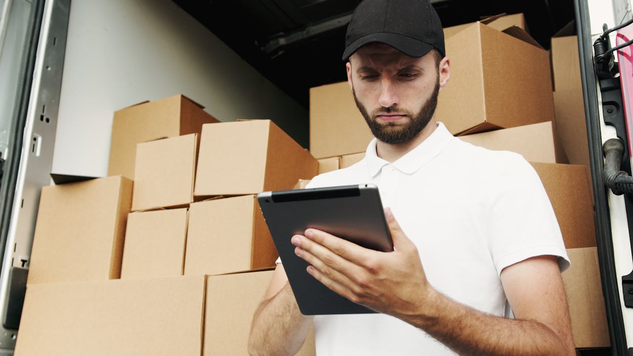 portfolio-03 Delivery worker using a tablet to manage shipments with stacked boxes in the background.
